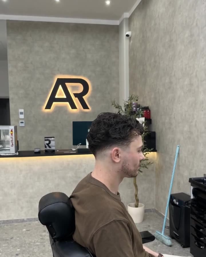 Kunde im Barbershop-Stuhl vor der beleuchteten Logowand des Salons